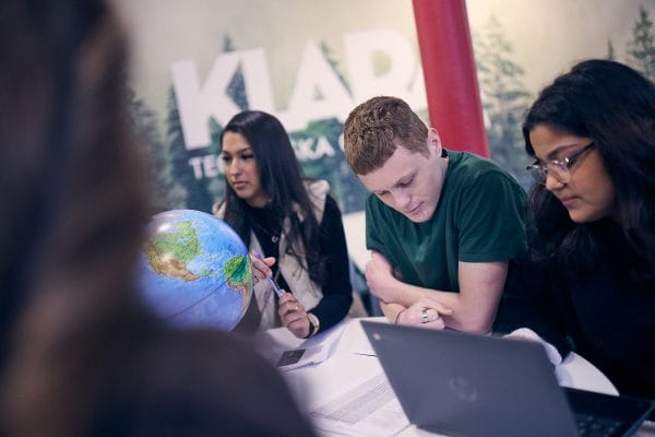 Tre elever sitter i skolan och diskuterar en gruppuppgift.