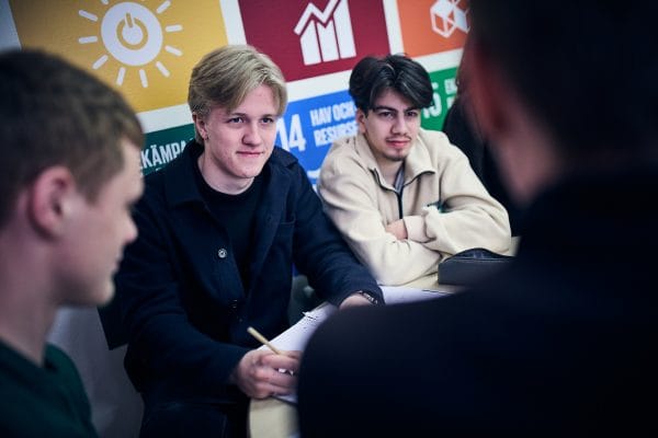 Tre elever sitter i skolan och får instruktioner av en gruppuppgift.