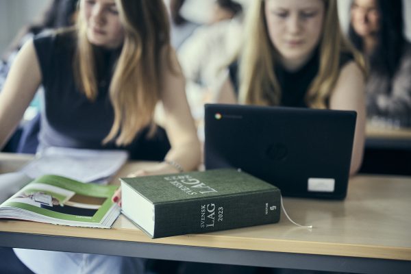 Studenter fokuserar med juridikbok och laptop.