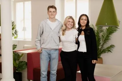 Tre elever står i skolan och ser glada ut och tittar in i kameran på KLARA.