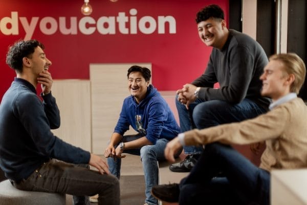 Killar sitter och skrattar framför en röd vägg med texten Edyoucation.