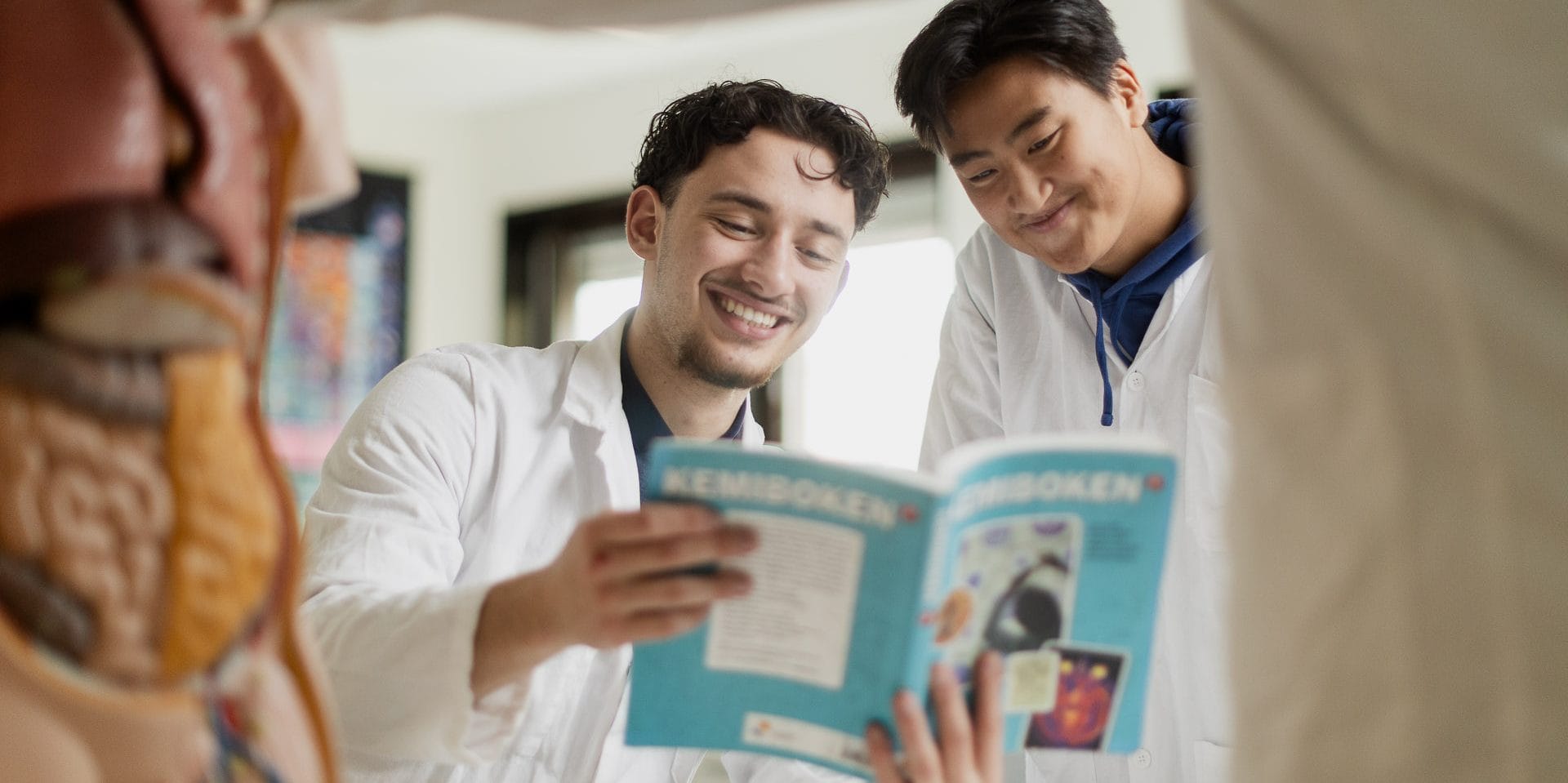 Två elever läser en bok iklädda vit labbrock.