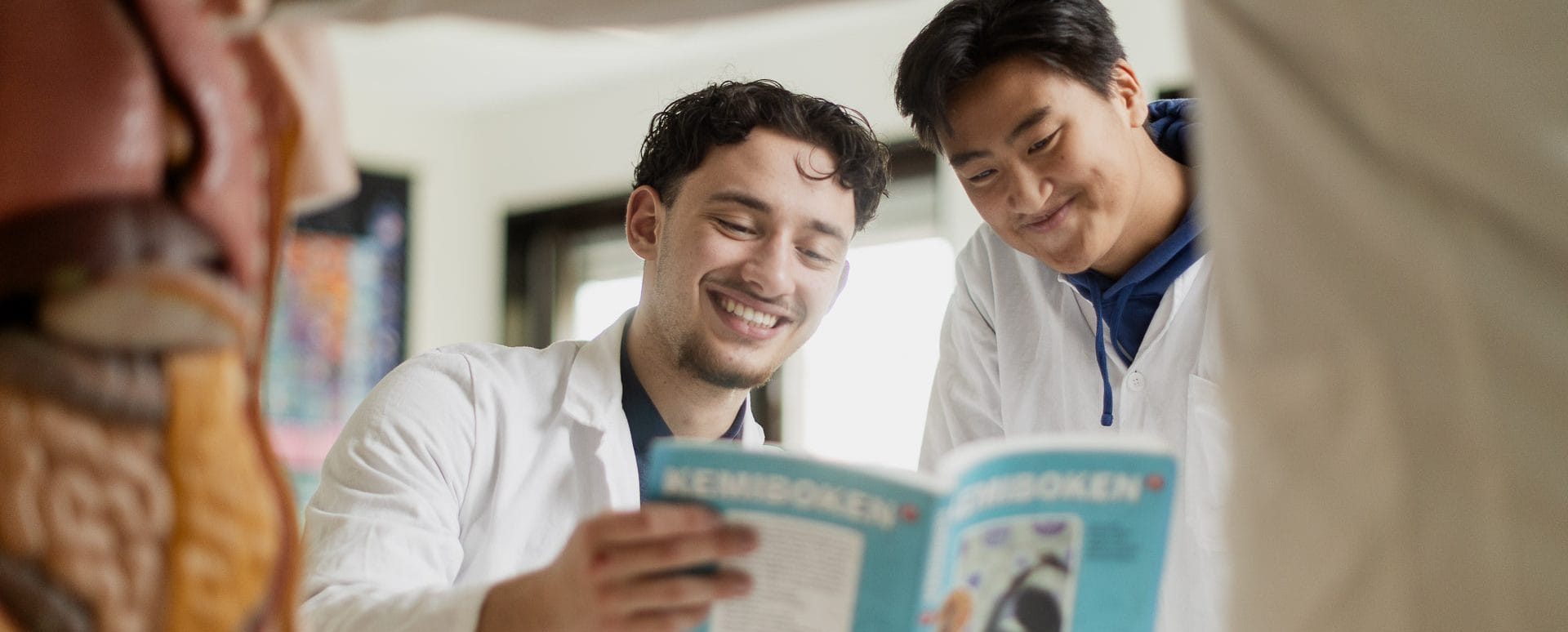 Två elever läser en bok iklädda vit labbrock.