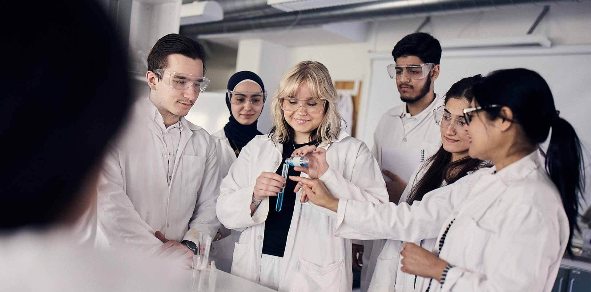 Elever i vita rockar och skyddsglasögon laborerar