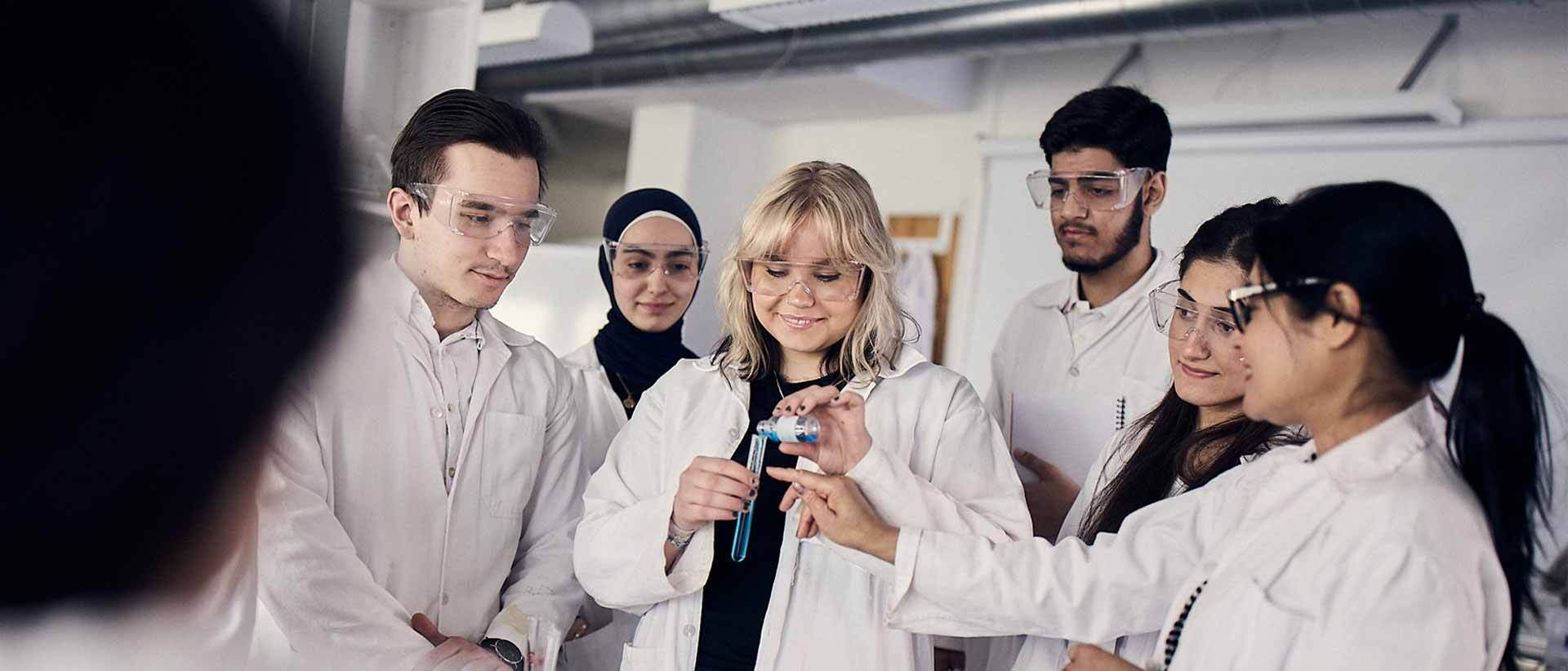 Elever i vita rockar och skyddsglasögon under en laboration