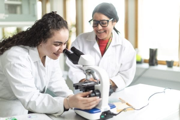 Elev tittar i mikroskop och får hjälp av lärare.