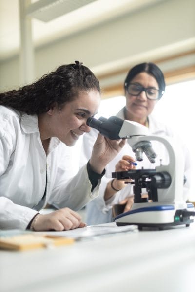Elev tittar i mikroskop och får hjälp av sin lärare.