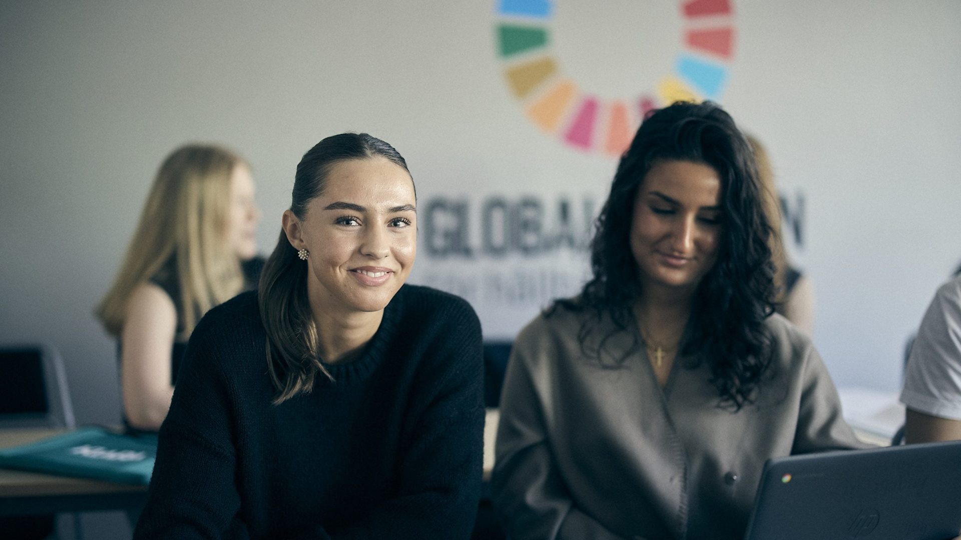 Två elever samarbetar med laptop och bok.