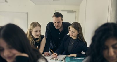 Lärare hjälper två elever med uppgift.