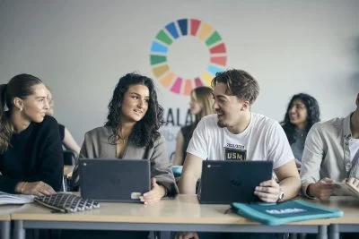 Elever samarbetar med laptops i klassrum.