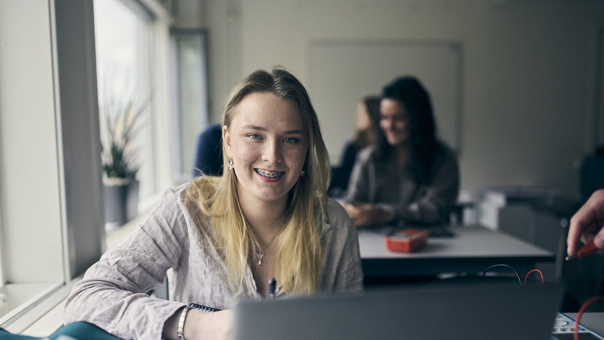 Student med laptop leende i klassrum.